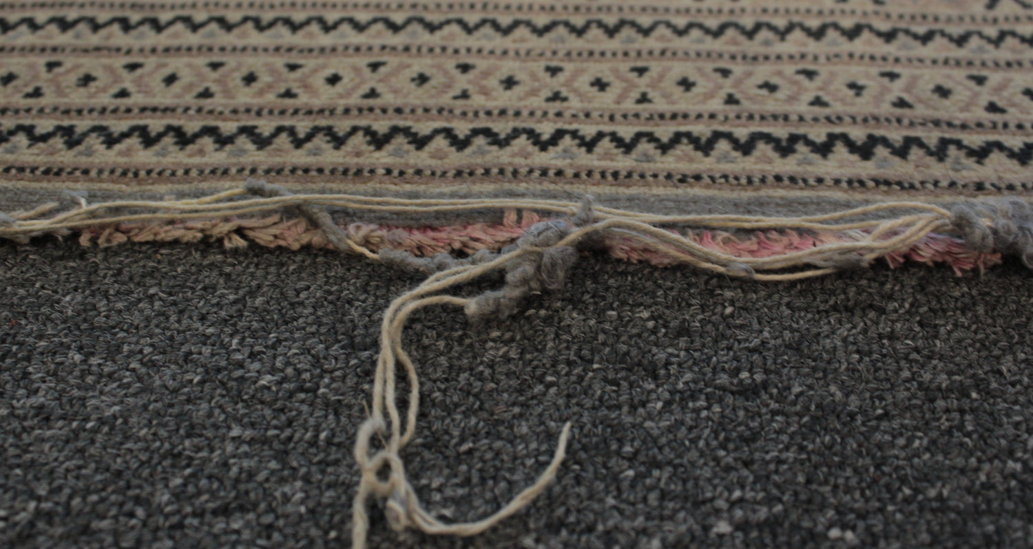A hand knotted wool rug with a damaged edge that needs repair.